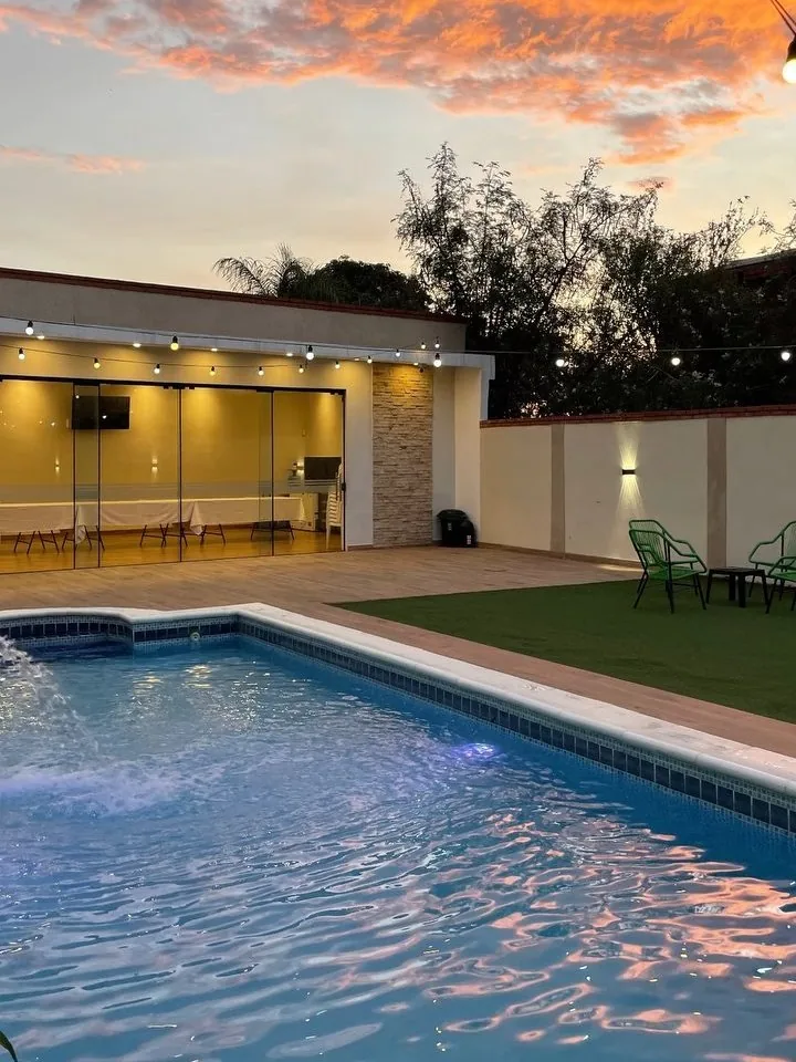 Piscina de Quinta Ohana al atardecer, con el salón iluminado al fondo